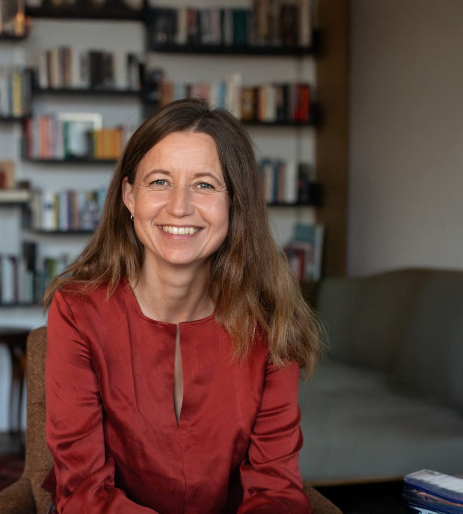 Porträt einer systemischen Therapeutin in Praxisumgebung mit Bücherregal im Hintergrund.